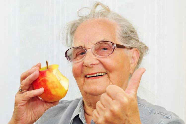 Eine ältere Frau zeigt Zustimmung, während sie einen Apfel in der Hand hält.